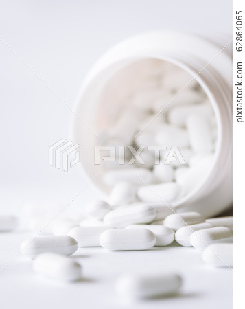 White pills spilled out of a plastic jar. Medicine capsules on white background. White pills spilled out of a plastic jar. Medicine capsules on white background. 62864065
