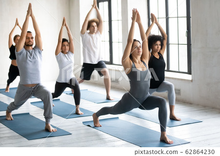 Young people practicing yoga doing Warrior one exercise 62864230