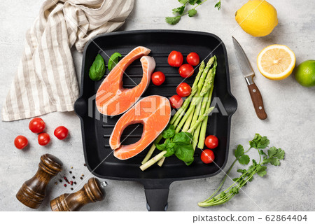 Uncooked salmon steaks with vegetables on a grill pan 62864404