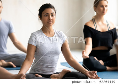 Indian woman with associates meditating seated cross-legged on mats Indian woman with associates meditating seated cross-legged on mats 62864449