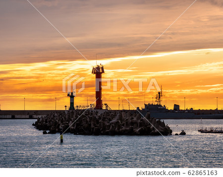 Beautiful sunset over Black sea and lighthouse in port of Sochi, Russia. Silhouettes of seagulls on rocks and tranquil sea surf. 62865163