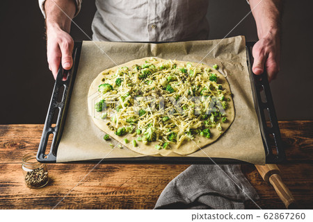 Man holding uncooked pizza with broccoli and cheese Man holding uncooked pizza with broccoli and cheese 62867260