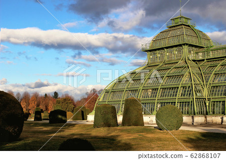 Green glasshouse, palm house in Dutch garden near Schoenbrunn palace, former imperial summer residence, Vienna, Austria, Europe. UNESCO Travel concept. Decorative trees and lawn in park. Green glasshouse, palm house in Dutch garden near Schoenbrunn palace, former imperial summer residence, Vienna, Austria, Europe. UNESCO Travel concept. Decorative trees and lawn in park. 62868107