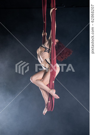 Female athletic, sexy and flexible aerial circus artist with redhead dancing in the air on the silk 62868207