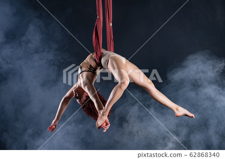 Female athletic, sexy and flexible aerial circus artist with redhead dancing in the air on the silk Female athletic, sexy and flexible aerial circus artist with redhead dancing in the air on the silk 62868340