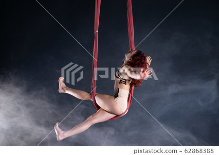 Female athletic, sexy and flexible aerial circus artist with redhead dancing in the air on the silk 62868388