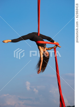 Beautiful and flexible female circus artist dancing with aerial silk on a sky background 62868418