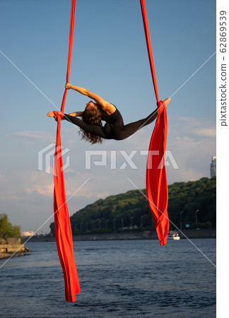 Beautiful and flexible female circus artist dancing with aerial silk with sky and river coastline on 62869539