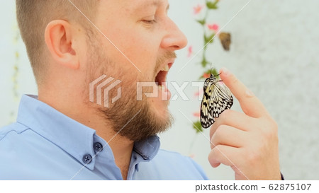 male holds a butterfly in his hand and wants to eat an insect, joke, close-up male holds a butterfly in his hand and wants to eat an insect, joke, close-up 62875107