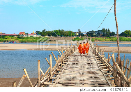 Three buddhist monks on bamboo bridge across 62879841