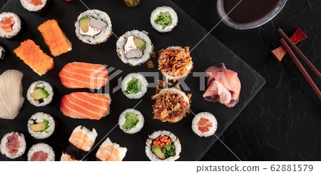Large sushi set panorama with soy sauce and chopsticks, shot from above on a black background. An assortment of various maki, nigiri and rolls 62881579