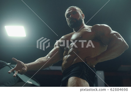 Bodybuilder strong man pumping up abs muscles 62884698