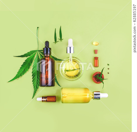 Glass bottles with CBD oil, THC tincture and hemp leaves on green background. Flat lay, minimalism. Cosmetics CBD hemp oil. 62885197