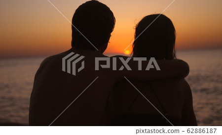 Romantic couple relaxing enjoying on beach looking at sunset 62886187