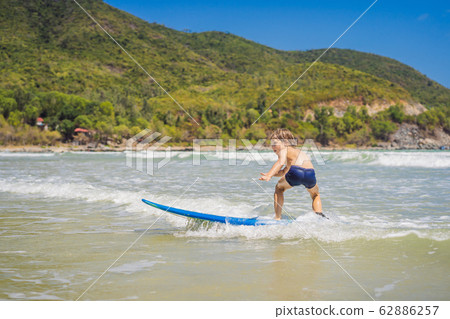 Healthy young boy learning to surf in the sea or ocean Healthy young boy learning to surf in the sea or ocean 62886257