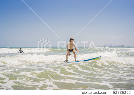 Healthy young boy learning to surf in the sea or ocean Healthy young boy learning to surf in the sea or ocean 62886263