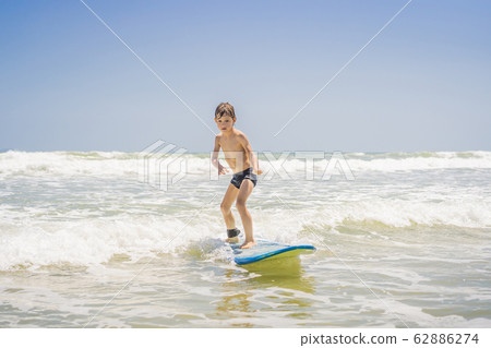 Healthy young boy learning to surf in the sea or ocean Healthy young boy learning to surf in the sea or ocean 62886274