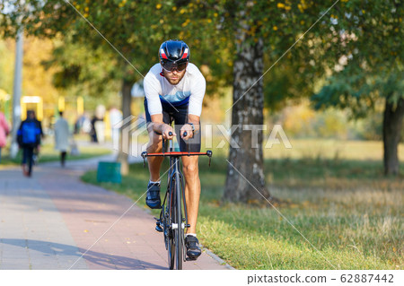 Young triathlete sportsman riding bicycle on road 62887442