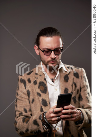 Man in sunglasses in jacket with phone in his hands on brown background Man in sunglasses in jacket with phone in his hands on brown background 62890540