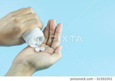 Woman holding white pills on hand against blue Woman holding white pills on hand against blue 62892002
