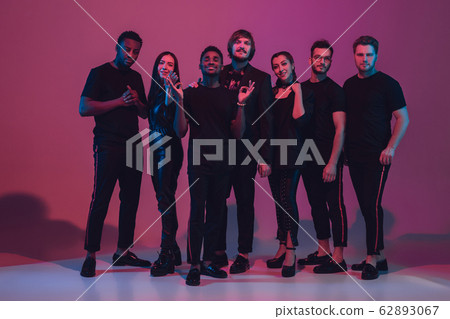 Group of young multiethnic musicians created band, dancing in neon light on pink background 62893067