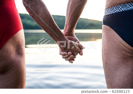 Midsection of senior couple in swimsuit by lake outdoors before swimming. 62898125