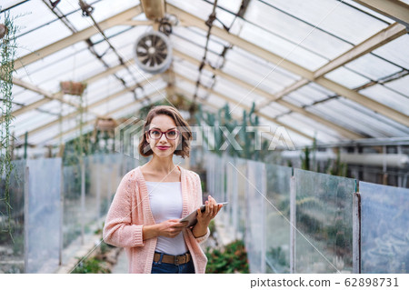 Young woman researcher standing in greenhouse, using tablet. 62898731