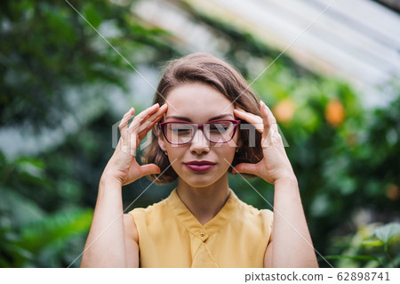 Tired young woman standing in greenhouse in botanical garden. 62898741