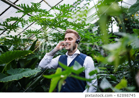Young man with headphones standing in botanical garden. 62898745