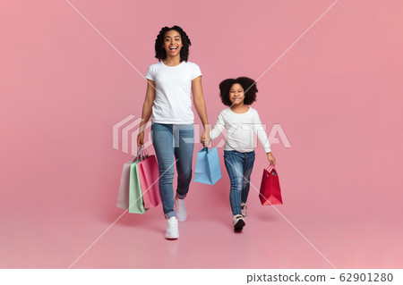 Black Mother And Daughter Walking With Shopping Bags On Pink Background 62901280