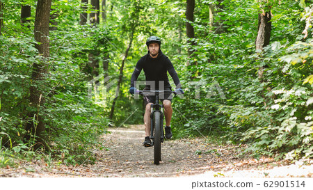 Motivated professional cyclist riding bike along forest road Motivated professional cyclist riding bike along forest road 62901514