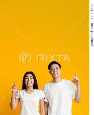 Excited asian man and woman pointing upwards 62901589