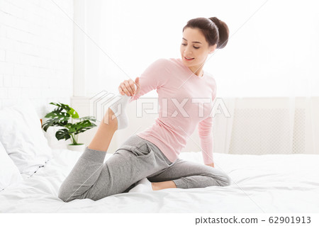 Young woman stretching her legs, exercising in bed Young woman stretching her legs, exercising in bed 62901913