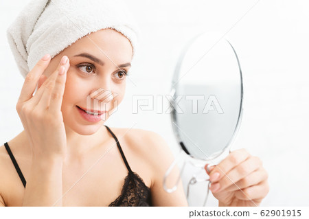Millennial woman massaging her face, looking at mirror Millennial woman massaging her face, looking at mirror 62901915
