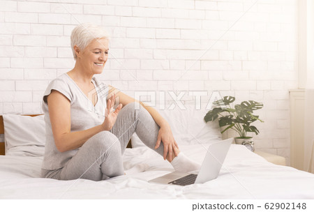 Cheerful senior lady talking with friends on laptop online Cheerful senior lady talking with friends on laptop online 62902148
