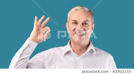 Smiling elderly man gesturing ok sign at blue studio Smiling elderly man gesturing ok sign at blue studio 62902150