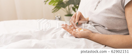 Senior lady holding lots of pills in hand in bed 62902151