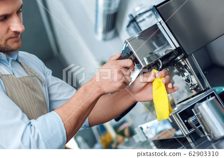 Coffee Passion. Young barista at coffee shop cleaning steamer concentrated close-up 62903310