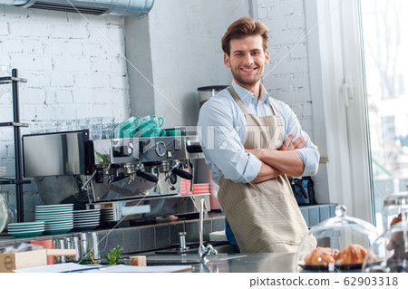 Coffee Passion. Young barista at coffee shop leaning back on counter crossed arms smiling confident 62903318