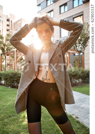 Urban Style. Young stylish woman in coat standing outdoors messing hair confident in sunlight 62903337