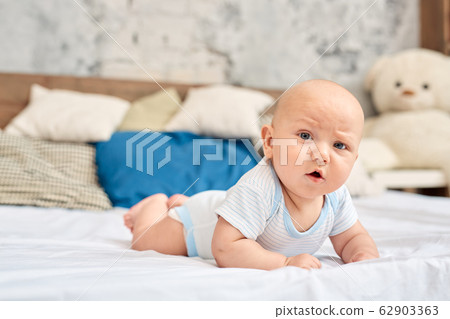 Funny little newborn baby lying on bed, looking at camera 62903363