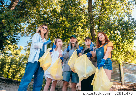 Group of activists friends collecting plastic waste on the beach. Guys show thumb up. 62911476