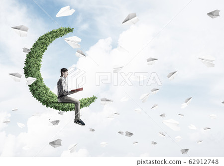 Handsome student guy sitting on green moon and reading book Handsome student guy sitting on green moon and reading book 62912748