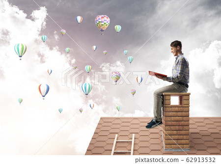 Handsome student guy reading book and aerostats flying in air Handsome student guy reading book and aerostats flying in air 62913532