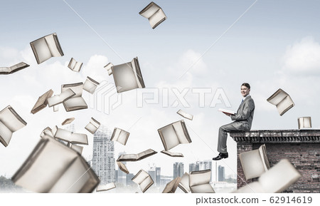 Man on roof reading book and many of them flying in air 62914619