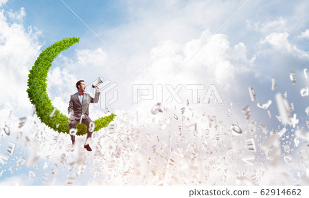 Businessman announcing something in loudspeaker and symbols fly around in air Businessman announcing something in loudspeaker and symbols fly around in air 62914662