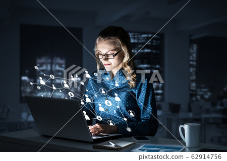 Attractive blonde wearing glasses in dark office using laptop. M Attractive blonde wearing glasses in dark office using laptop. M 62914756