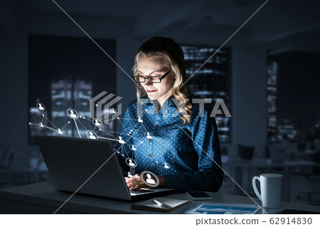 Attractive blonde wearing glasses in dark office using laptop. M Attractive blonde wearing glasses in dark office using laptop. M 62914830