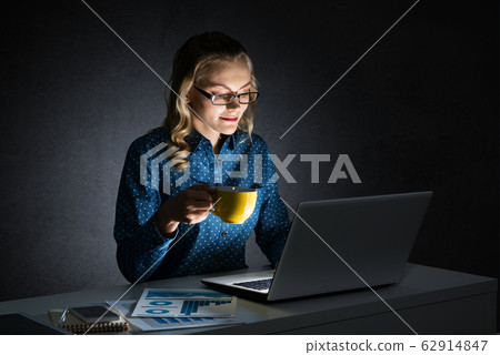 Attractive blonde working on laptop in dark office. Mixed media Attractive blonde working on laptop in dark office. Mixed media 62914847