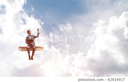 Young businessman or student floating in blue sky and studying the science Young businessman or student floating in blue sky and studying the science 62914917